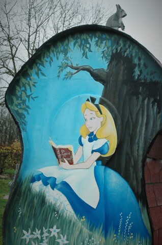 Boite au livres avec peint dessus Alice aux Pays des Merveilles lisant et un petit ecureuil en top 
